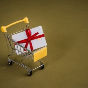 A gift card with a red bow sits in a mini shopping cart on a yellow backdrop.